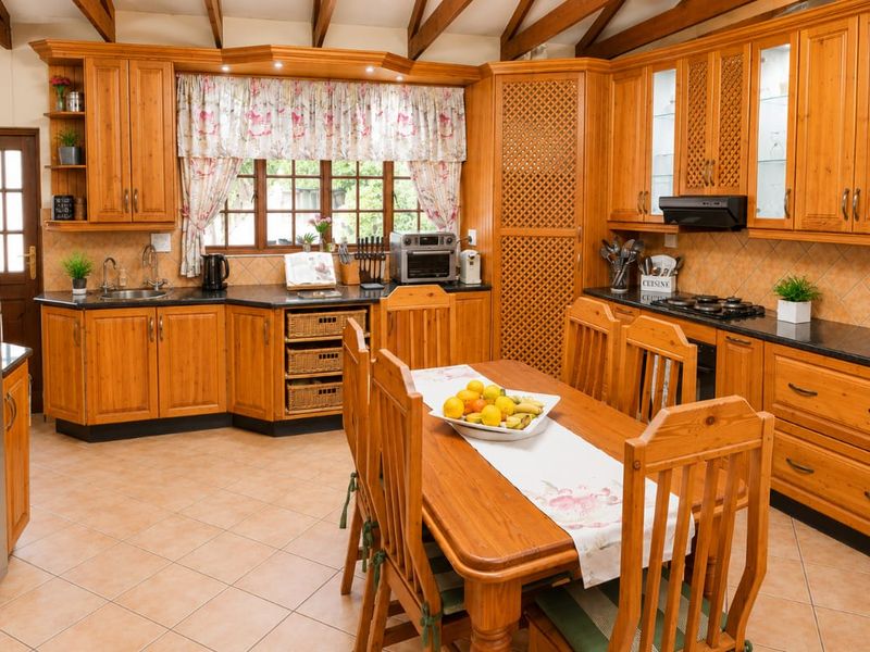 Spacious open-plan kitchen featuring warm timber cabinetry, granite countertops, gas hob, and exposed timber ceiling beams, creating a traditional and functional cooking space.