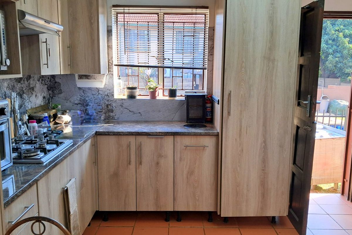 A functional kitchen featuring light wood-finish cabinetry, granite countertops, a gas hob, and built-in oven, with direct access to the outdoor area.