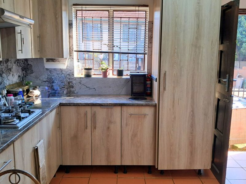 A functional kitchen featuring light wood-finish cabinetry, granite countertops, a gas hob, and built-in oven, with direct access to the outdoor area.