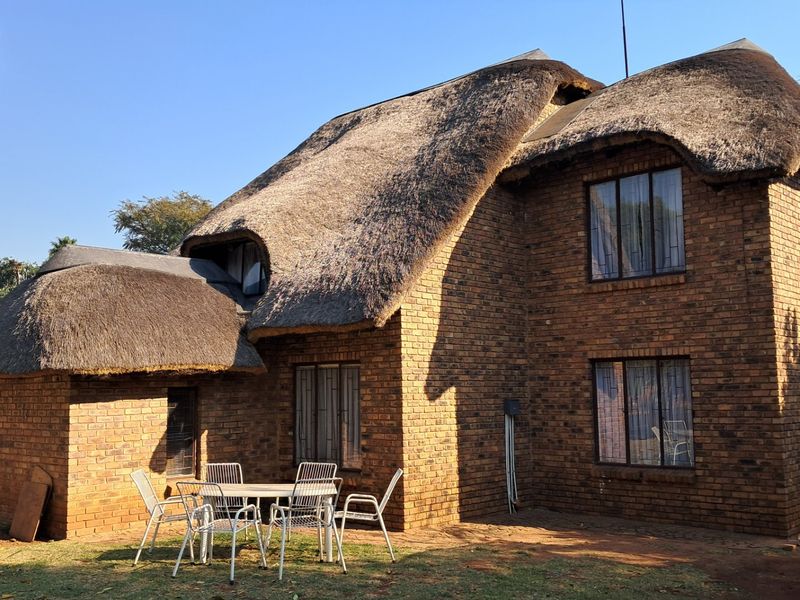 Rear view of a double-story facebrick house featuring a traditional thatch roof and secure window installations.