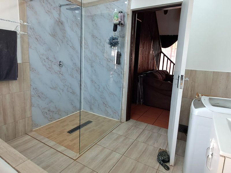 A modern bathroom featuring a walk-in shower with marble-look wall cladding, a glass screen, and tiled flooring.