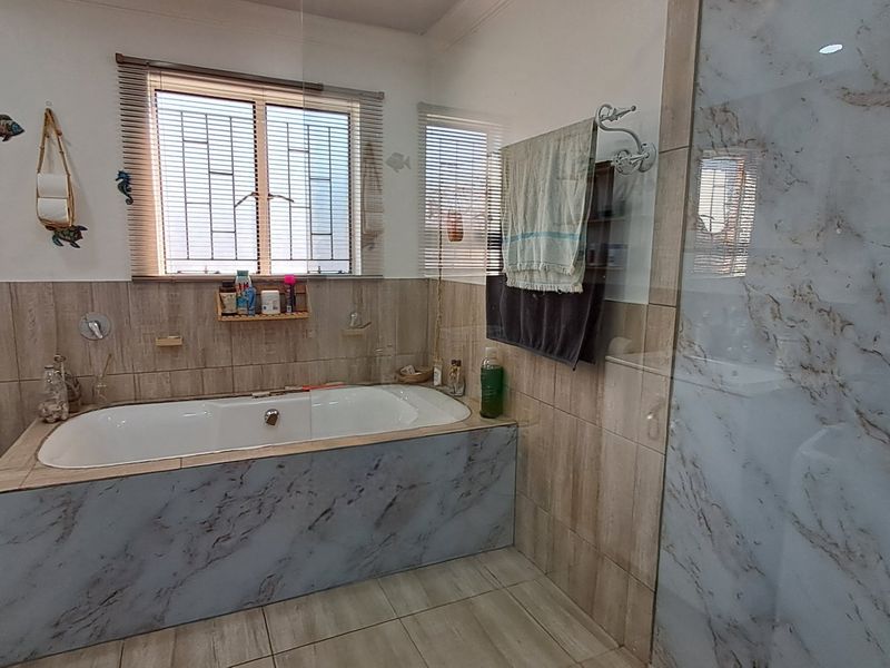 A well-maintained bathroom featuring a built-in bathtub, a separate walk-in shower with marble-effect tiling, and neutral floor tiles.