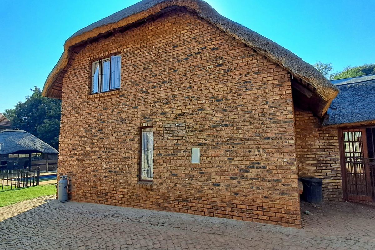 Rear view of a double-story face brick house featuring a traditional thatch roof, paved exterior area, and secure metal gate access.