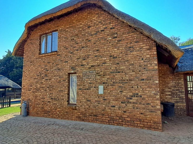 Rear view of a double-story face brick house featuring a traditional thatch roof, paved exterior area, and secure metal gate access.