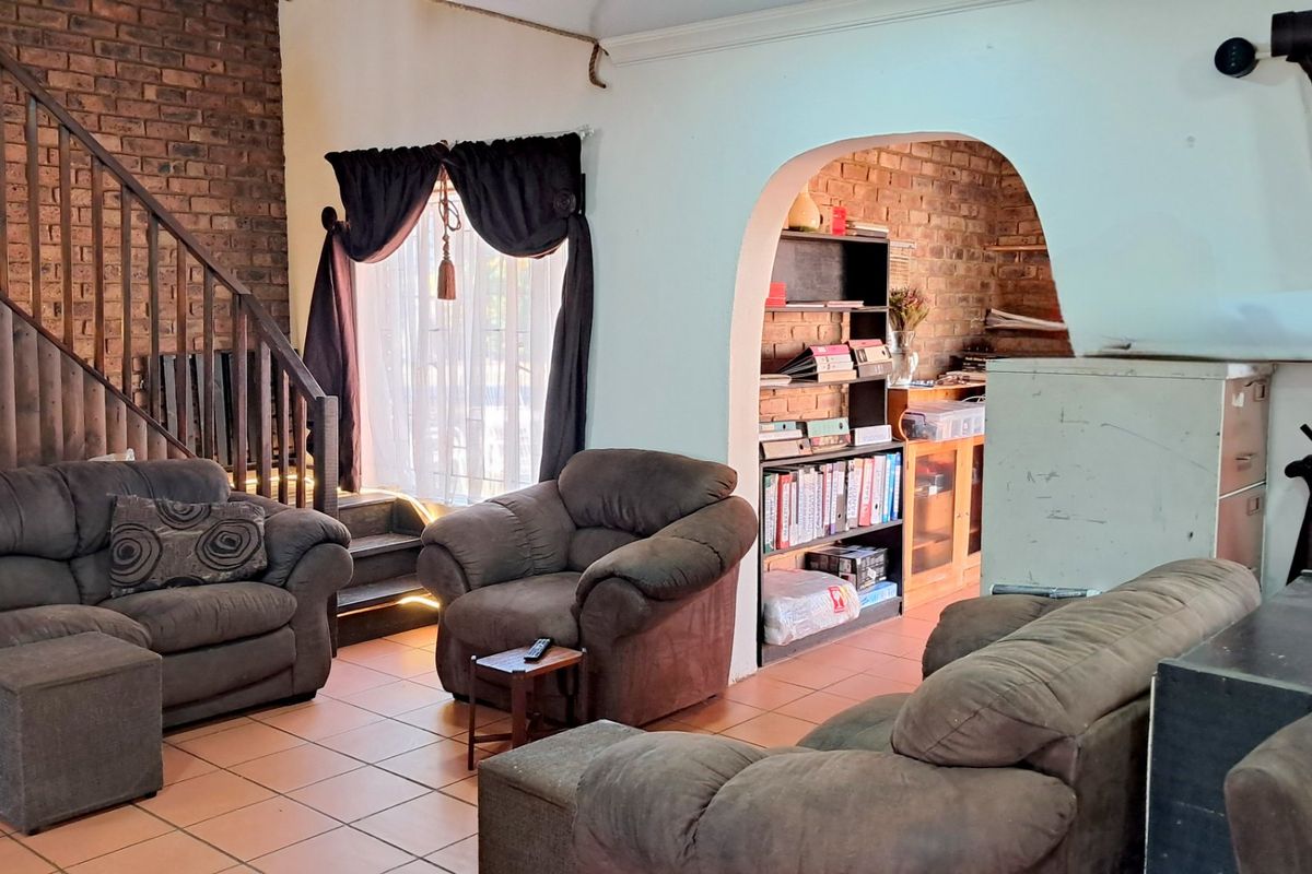 Spacious living area featuring exposed brick walls, tiled flooring, and a wooden staircase leading to the upper level.