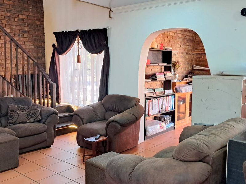 Spacious living area featuring exposed brick walls, tiled flooring, and a wooden staircase leading to the upper level.