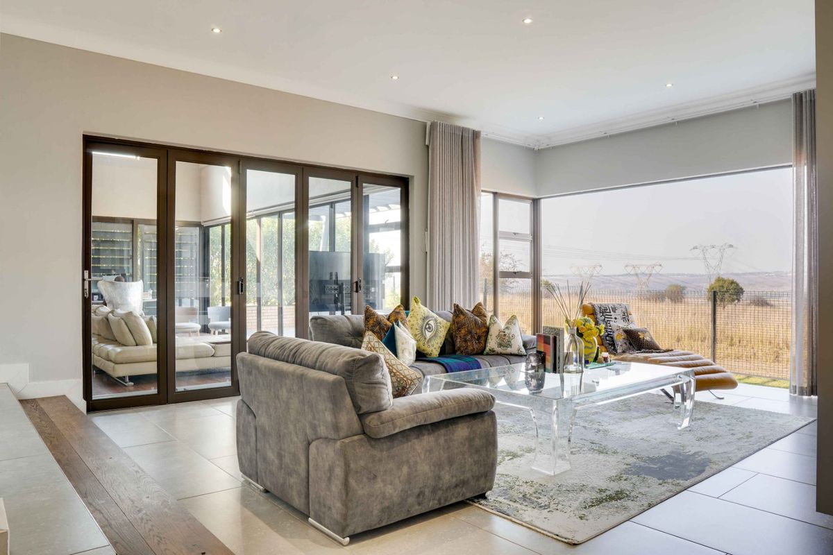 Spacious living room featuring large aluminium sliding doors, expansive corner windows, and modern recessed lighting, offering seamless indoor-outdoor flow and natural light.