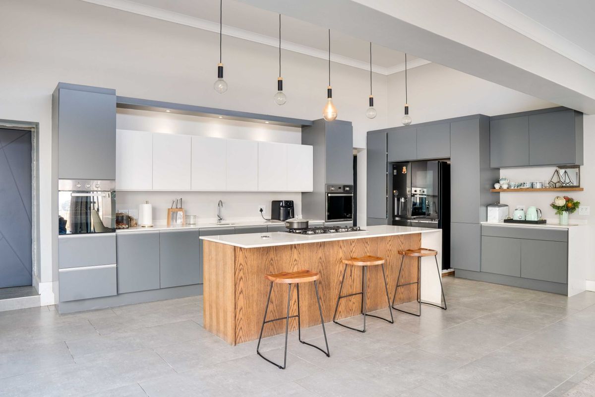 Modern kitchen featuring two-tone cabinetry, a central wooden island with stone countertop, built-in appliances, and contemporary pendant lighting.