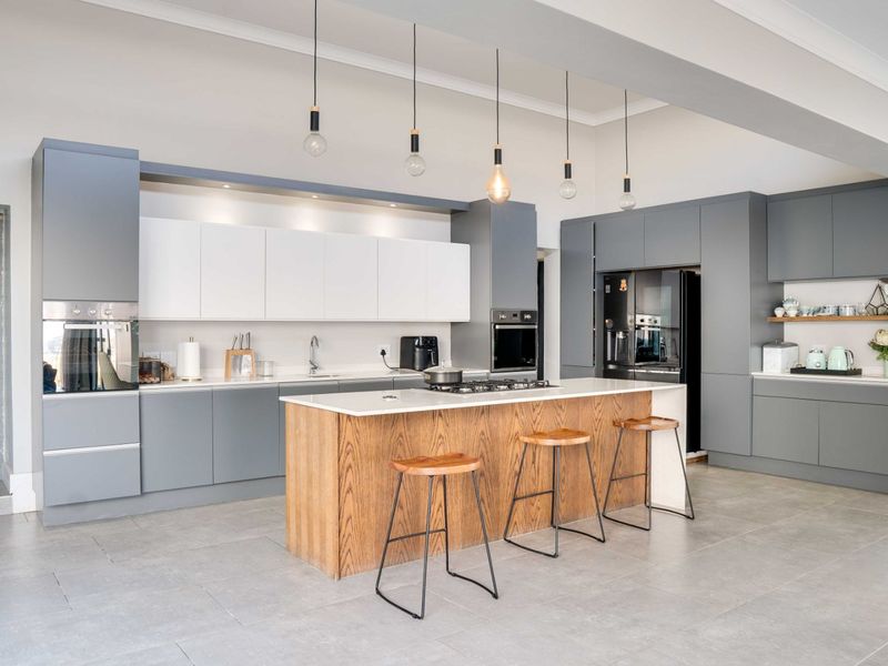 Modern kitchen featuring two-tone cabinetry, a central wooden island with stone countertop, built-in appliances, and contemporary pendant lighting.