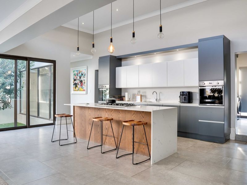 Modern open-plan kitchen featuring a large island with stone countertops, built-in appliances, sleek cabinetry, and direct access to an outdoor area through sliding doors.