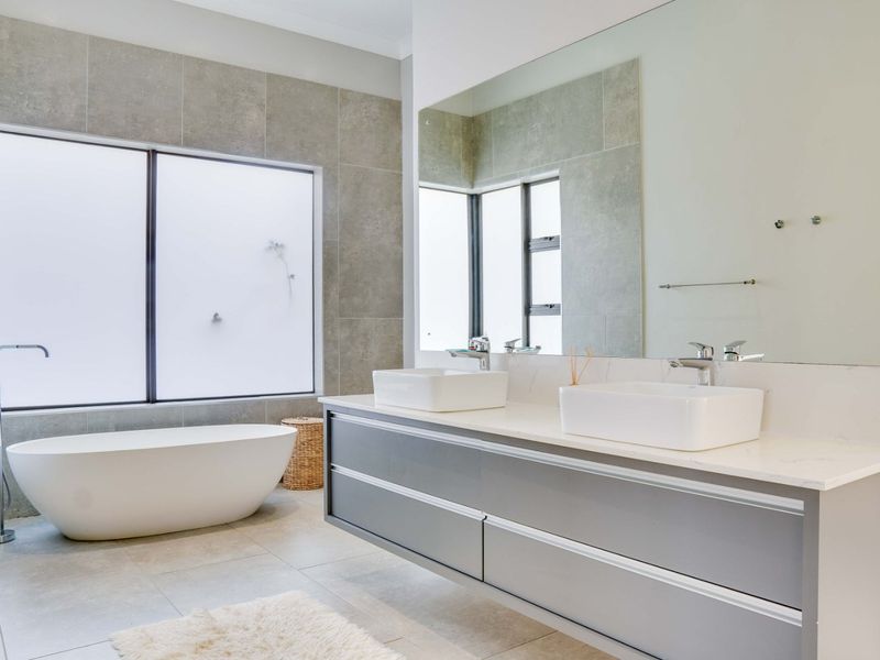Modern bathroom featuring a sleek double vanity, large wall mirror, and a contemporary freestanding bathtub with floor-to-ceiling tiled finishes.