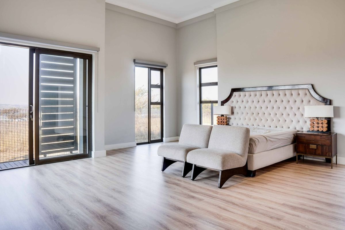 Spacious bedroom featuring light wood-look laminate flooring, neutral walls, and large sliding glass doors providing ample natural light and outdoor access.
