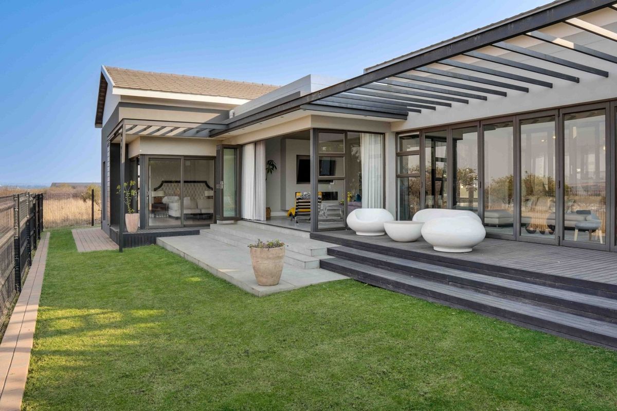 A modern rear exterior view featuring a spacious timber deck, pergola, and large sliding glass doors that provide seamless indoor-outdoor flow to the garden.