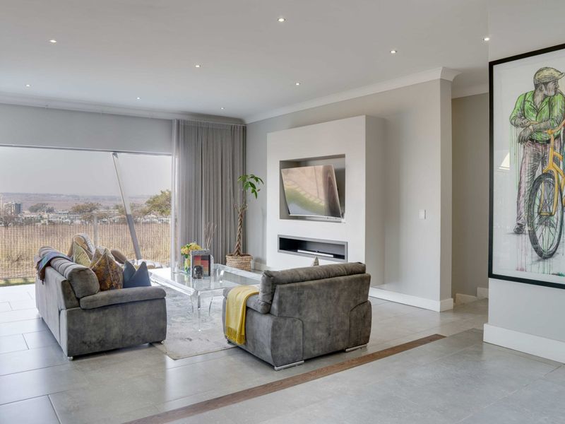 Modern living room featuring a sleek built-in media wall, recessed ceiling lighting, large format floor tiles, and expansive sliding doors with scenic views.