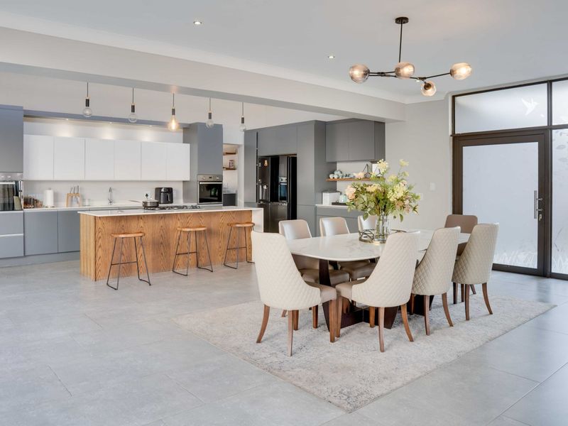 Modern open-plan kitchen and dining area featuring a large island, sleek cabinetry, integrated appliances, and contemporary lighting, finished with high-quality tiled flooring.