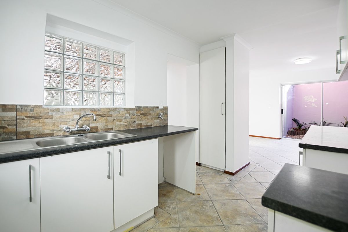 A functional kitchen featuring white cabinetry, laminate countertops, a double bowl sink, and a unique glass block window, leading to an open living area.