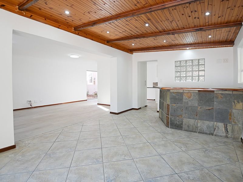 Spacious open-plan living area featuring a timber-clad ceiling, stone-accented breakfast bar, and a mix of ceramic tile and laminate flooring.