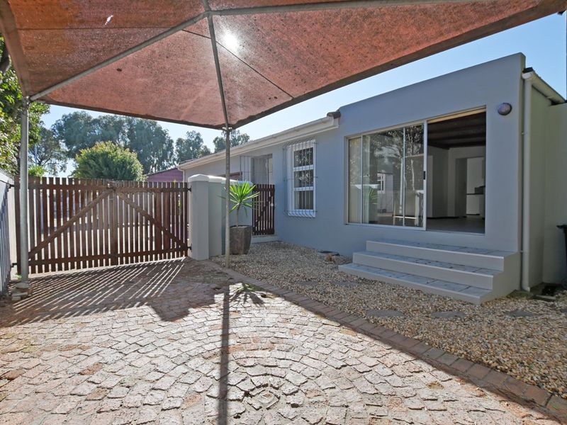 Rear exterior area featuring cobblestone paving, a gravel garden, a shade sail, and a sliding glass door providing access to the interior.