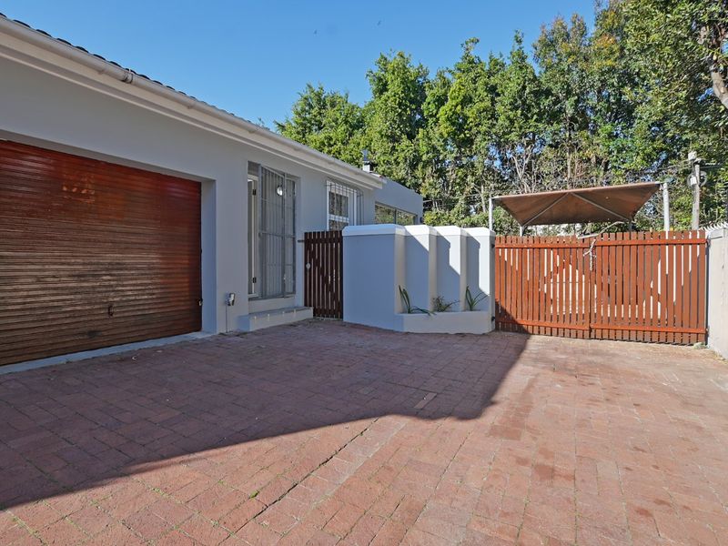 Front exterior view featuring a brick paved driveway, a roll-up garage door, and secure timber gate access to the property.