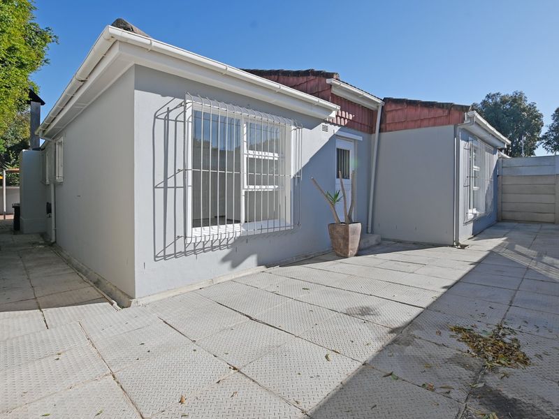 Rear exterior view of the house featuring a paved patio area, security bars on windows, and a tiled roof.