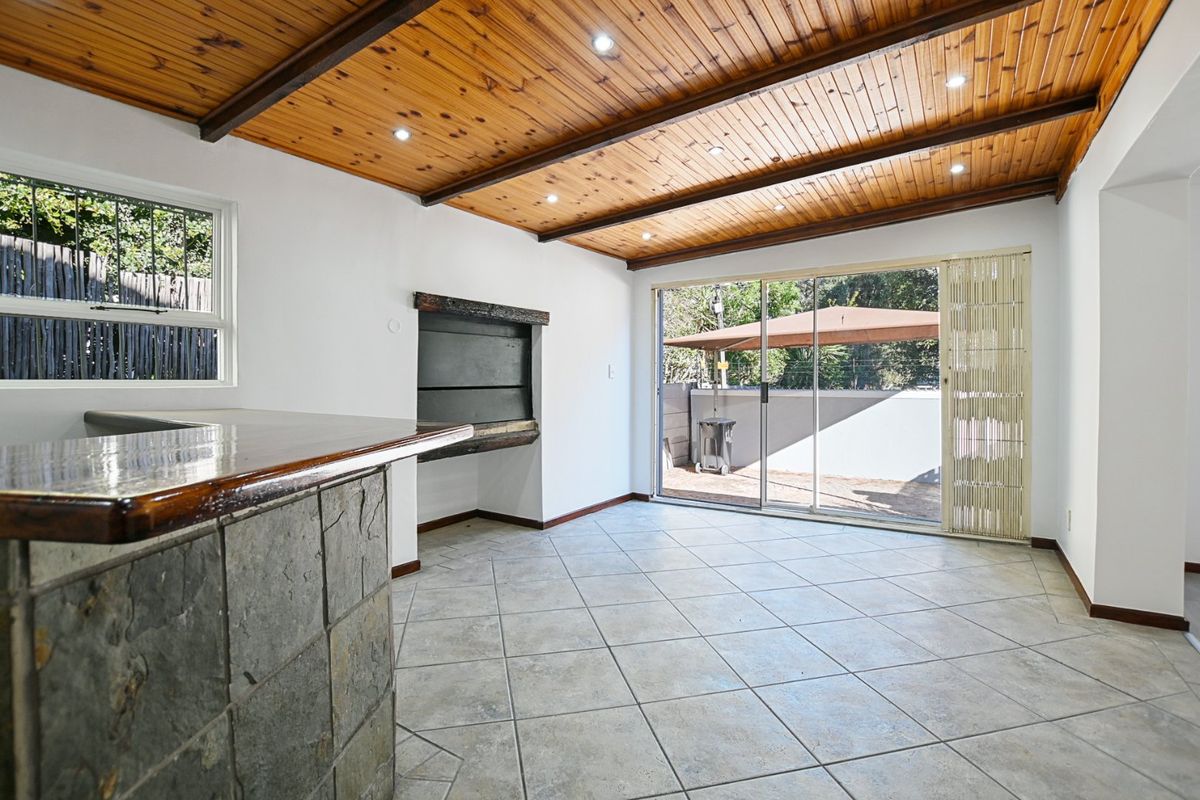 Spacious living area featuring a timber ceiling, built-in fireplace, stone-clad bar counter, and sliding glass doors leading to an outdoor patio.