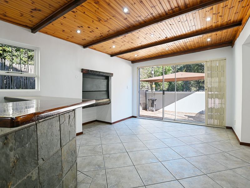 Spacious living area featuring a timber ceiling, built-in fireplace, stone-clad bar counter, and sliding glass doors leading to an outdoor patio.