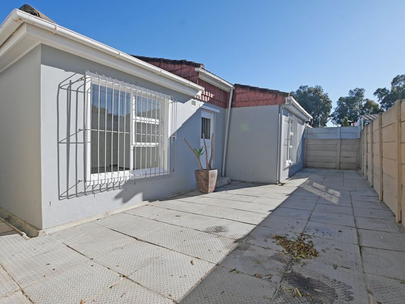 Rear exterior view of the property featuring a paved patio area, security bars on windows, and a precast concrete boundary wall.
