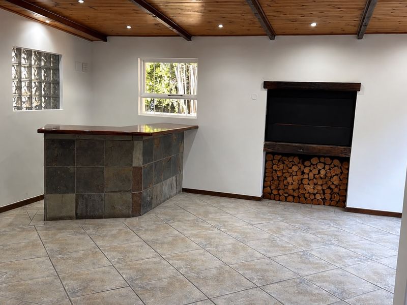 Spacious entertainment area featuring a built-in bar with stone cladding, a fireplace with integrated wood storage, and exposed timber ceiling beams.