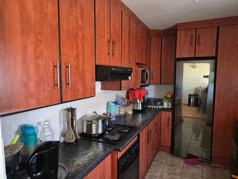 Functional kitchen featuring wood-look cabinetry, built-in oven and hob, tiled backsplash, and tiled flooring with ample storage space.