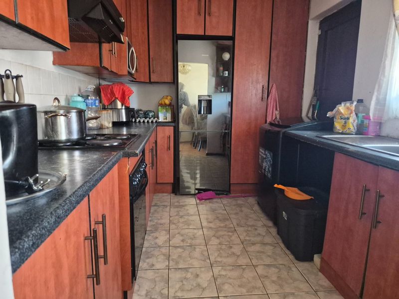 A functional kitchen featuring laminate cabinetry, tiled flooring, and built-in appliances, offering a practical layout with potential for modern cosmetic updates.