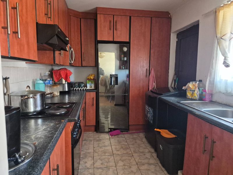 A functional kitchen featuring laminate cabinetry, dark countertops, built-in oven, electric hob, and a stainless steel sink with tiled flooring.