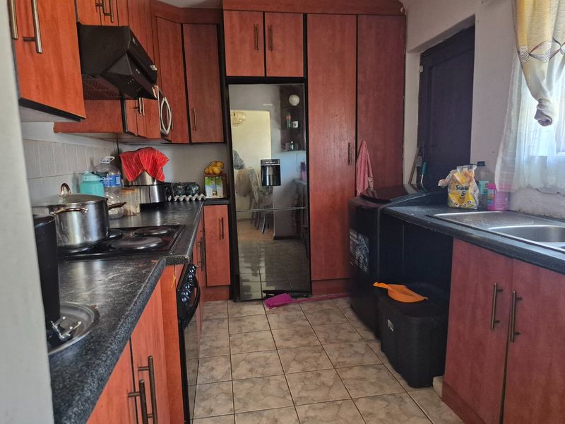 A functional kitchen featuring laminate cabinetry, dark countertops, an electric hob with extractor, and a stainless steel sink, offering potential for modern updates.