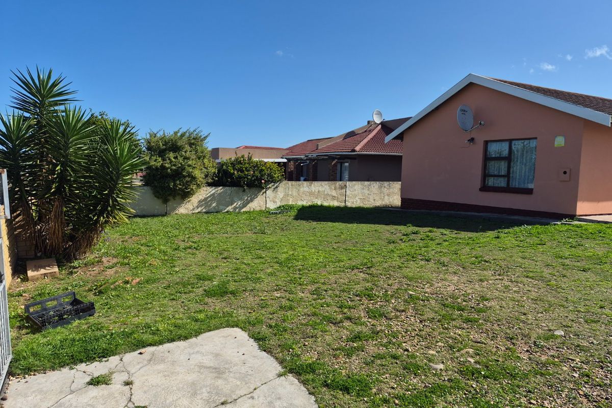 A rear garden area featuring a lawn, concrete paving, and a boundary wall, adjacent to the side elevation of the house.