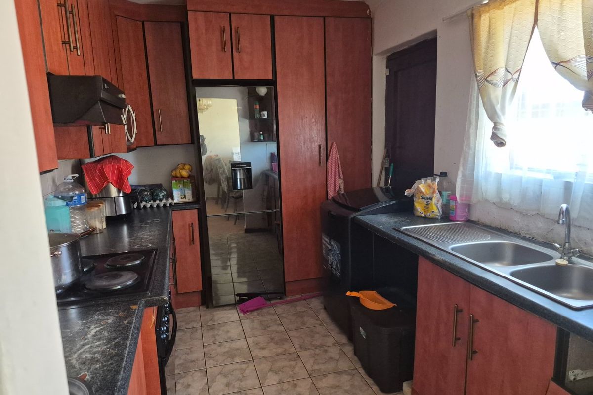 A functional kitchen featuring laminate cabinetry, dark countertops, a double bowl sink, and an integrated electric hob with an extractor fan.