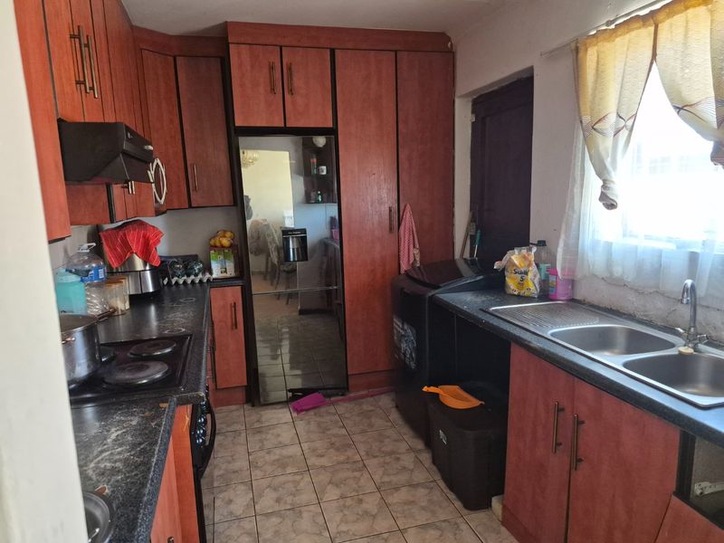 A functional kitchen featuring laminate cabinetry, dark countertops, a double bowl sink, and an integrated electric hob with an extractor fan.