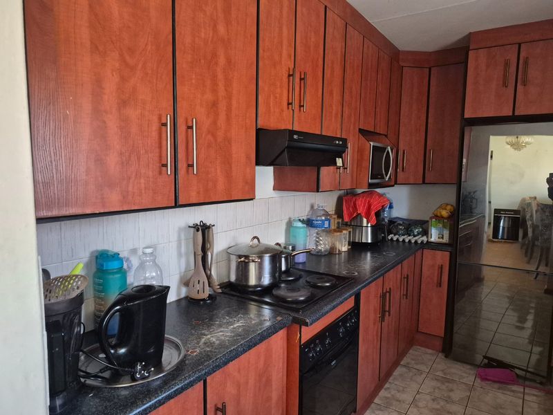 A functional kitchen featuring wood-look laminate cabinetry, dark countertops, built-in oven, electric hob, and tiled flooring, offering potential for modern updates.
