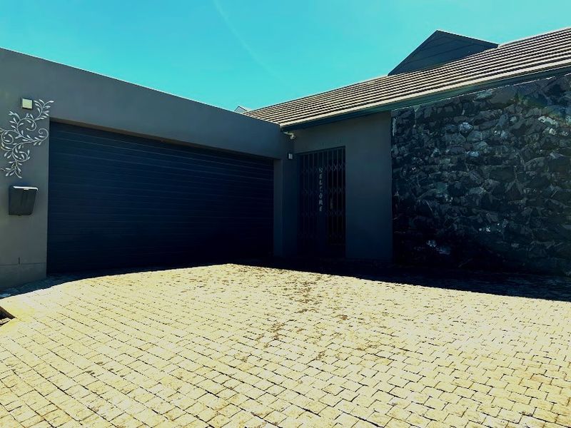 Front exterior view featuring a paved driveway, garage door, and stone-clad facade with a secure entrance gate.