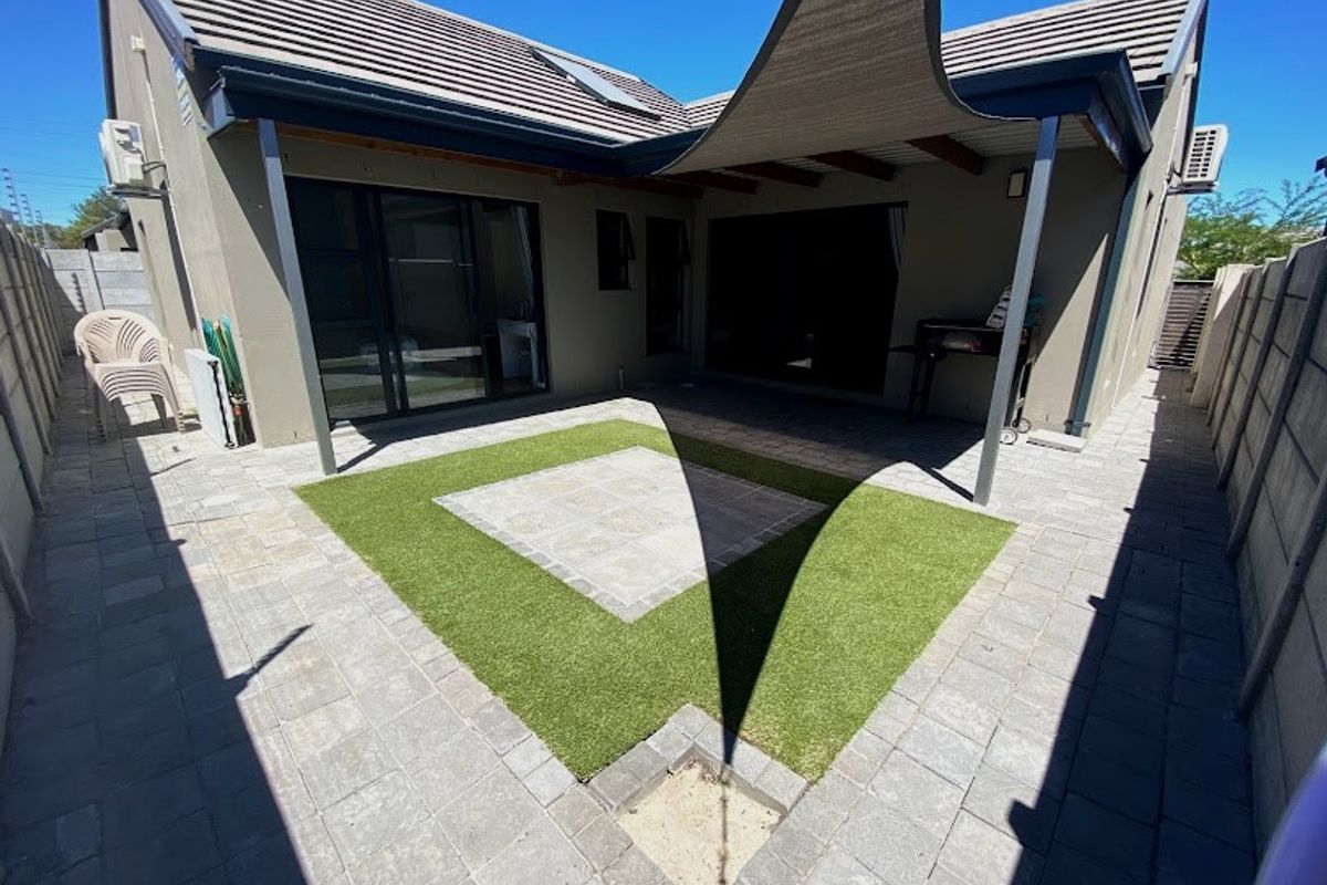 A well-maintained rear courtyard featuring a paved patio, artificial lawn, and a shade sail, providing a functional outdoor entertainment area.