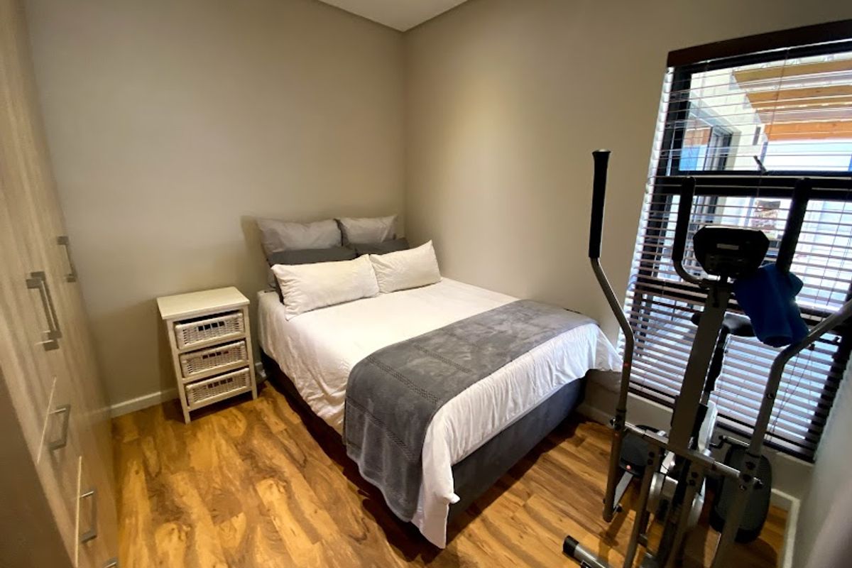 A well-maintained bedroom featuring laminate flooring, built-in cupboards, and venetian blinds, offering a clean and functional living space.