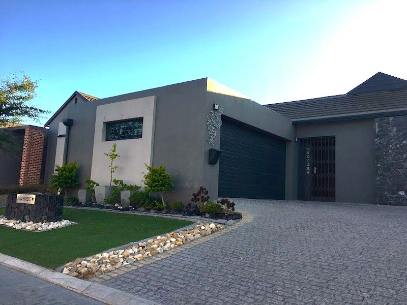Modern front elevation featuring a paved driveway, automated garage, and well-maintained landscaped garden with artificial lawn.