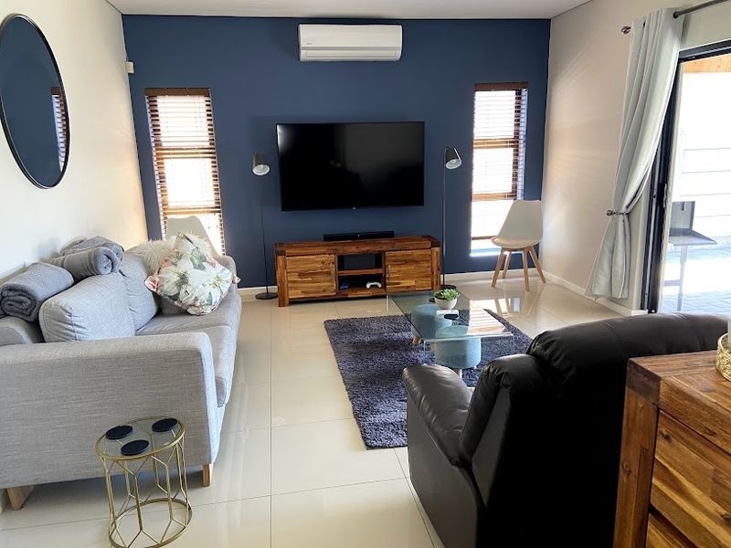 A well-maintained living room featuring polished tile flooring, a feature wall with a wall-mounted air conditioner, and access to an outdoor area.