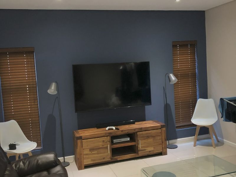 A living room featuring a dark blue accent wall, tiled flooring, recessed downlights, and dual windows fitted with wooden venetian blinds.