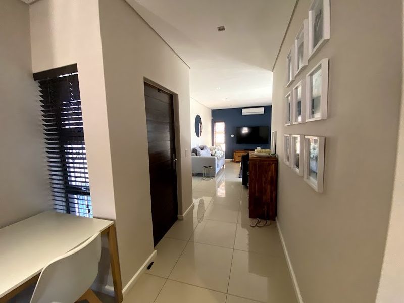 A bright, tiled hallway leading into an open-plan living area, featuring neutral walls, recessed lighting, and modern finishes throughout.