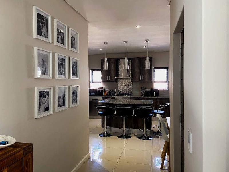 A modern kitchen featuring a central island, dark wood cabinetry, mosaic backsplash, and stylish pendant lighting, viewed from an adjacent hallway.