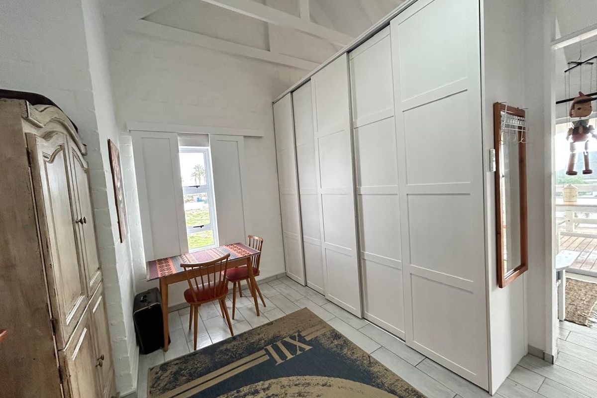 A bright bedroom featuring a high vaulted ceiling, large white built-in wardrobes, and tiled flooring with a window providing natural light.
