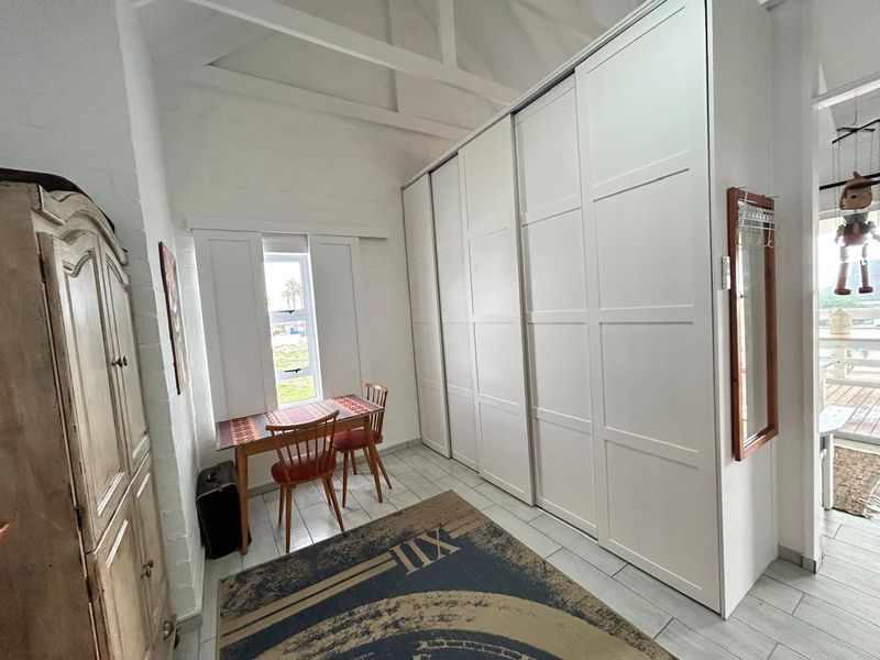 A bright bedroom featuring a high vaulted ceiling, large white built-in wardrobes, and tiled flooring with a window providing natural light.