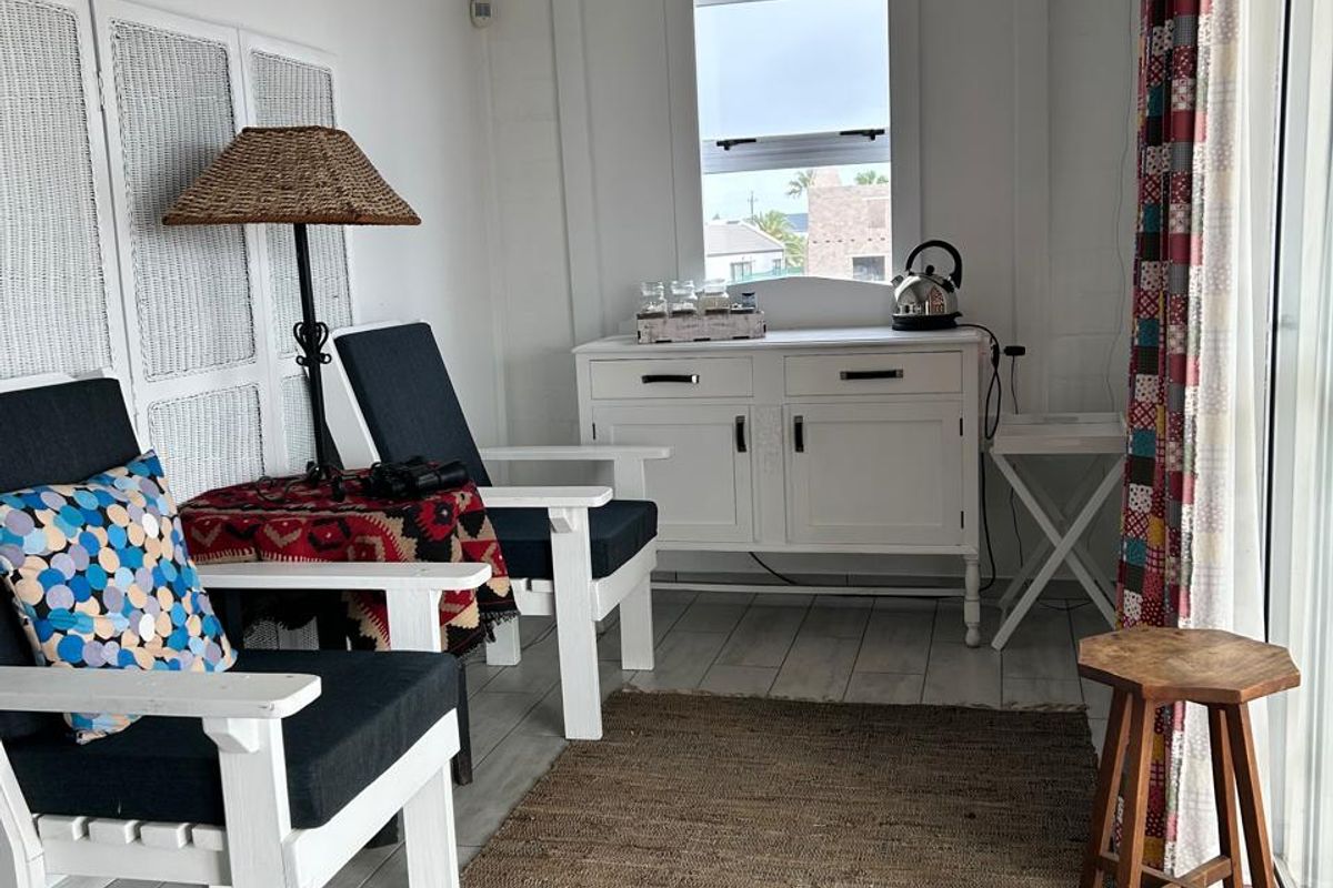 A bright, compact living area featuring white painted brick walls, tiled flooring, and a sliding glass door providing natural light.