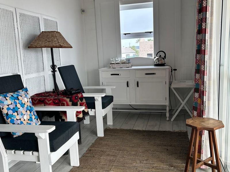 A bright, compact living area featuring white painted brick walls, tiled flooring, and a sliding glass door providing natural light.