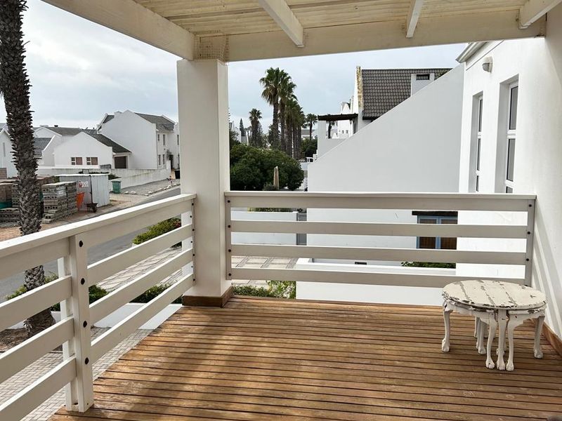 A covered balcony featuring timber decking and a white timber pergola, offering an outdoor space with views of the surrounding residential area.