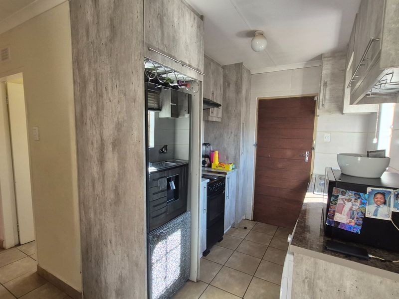 A functional kitchen featuring wood-look laminate cabinetry, tiled flooring, and a built-in stove with extractor fan, providing a practical workspace.
